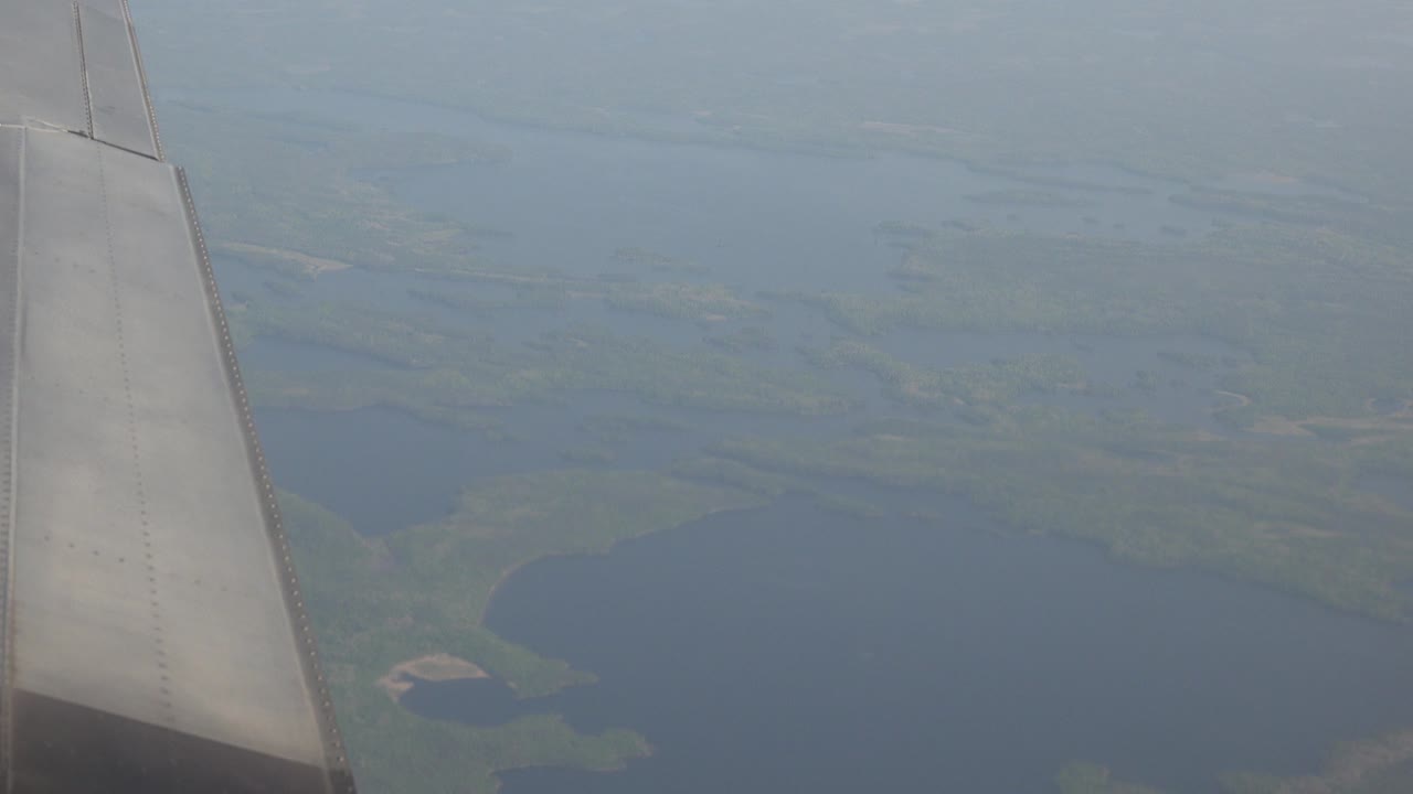 Passenger-window view over Red Lake, Canada with an airplane wing at left, hazy sky above lakes and green land, and no visible people.