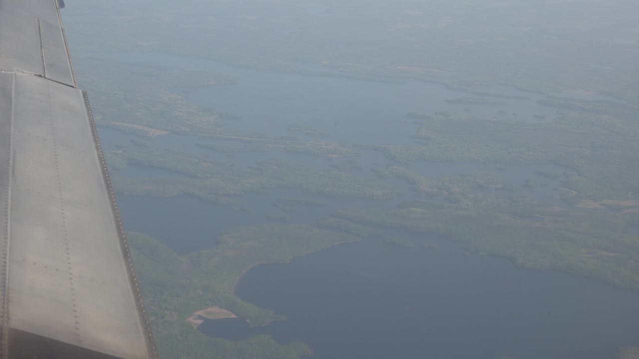 Aircraft wing over lake country with hazy blue distance