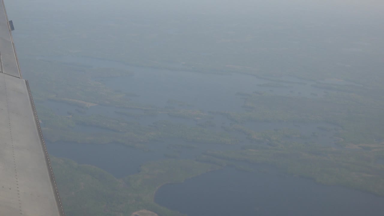 At the start of the Red Lake, Canada clip, an airplane wing sits along the left edge above hazy blue water and green land, with no visible people.