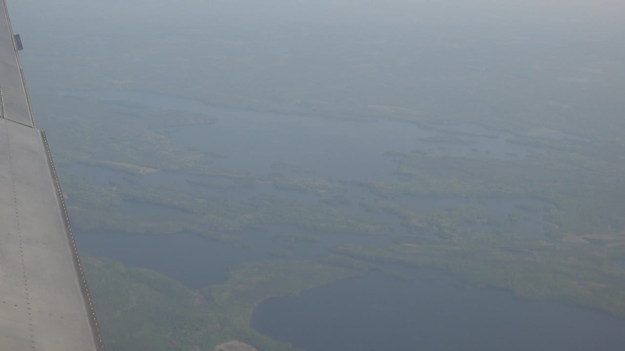 One second in, the aircraft wing is near the center-left of the frame, with pale sky above distant lake shapes and green shoreline in Red Lake, Canada, and no visible people.