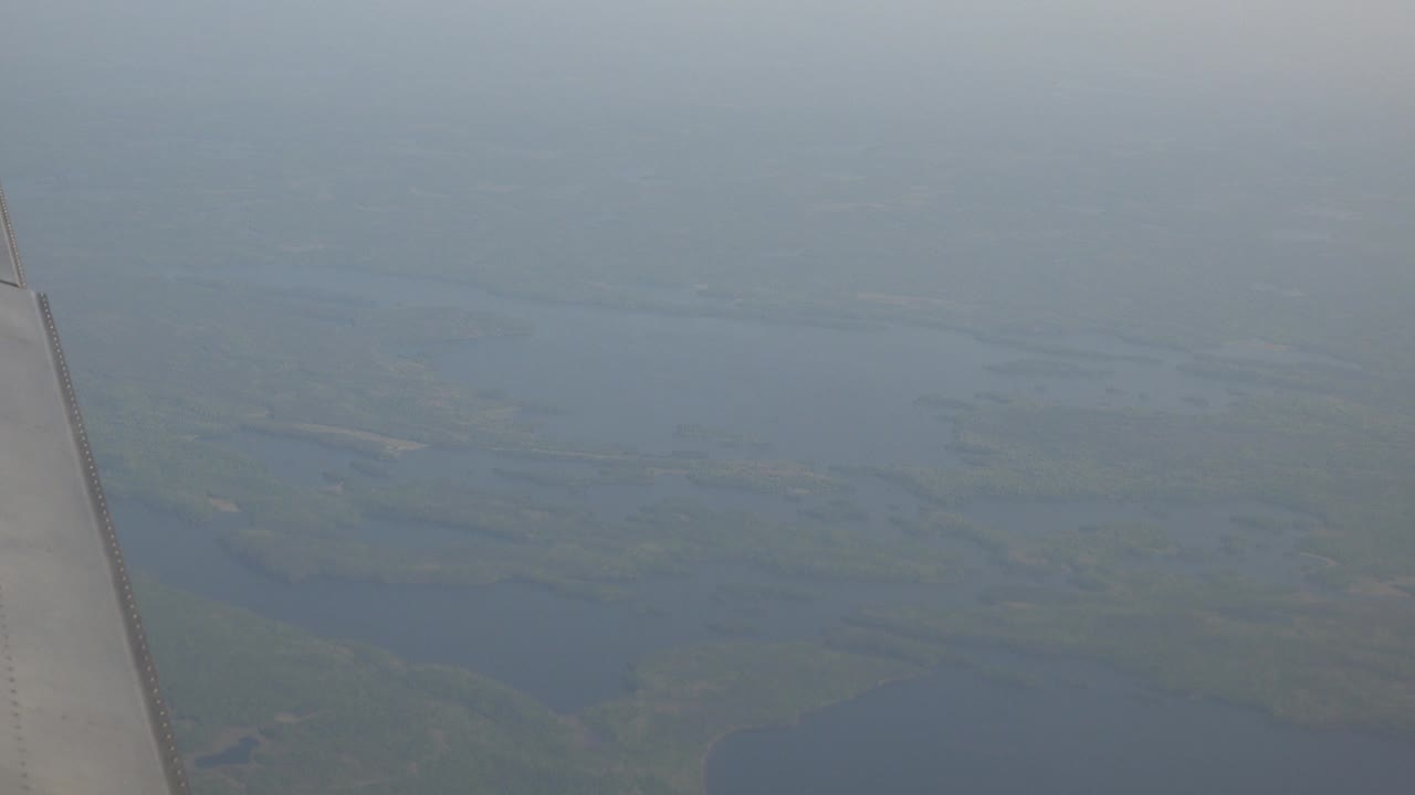A pale airplane wing crosses the left edge above hazy lakes and green vegetation in Red Lake, Canada, with no visible people.