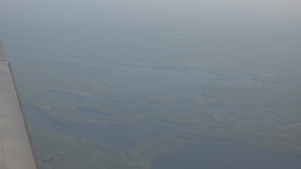 The airplane wing remains near the left side while muted blue lakes and green land spread across the hazy Red Lake, Canada view, with no visible people.