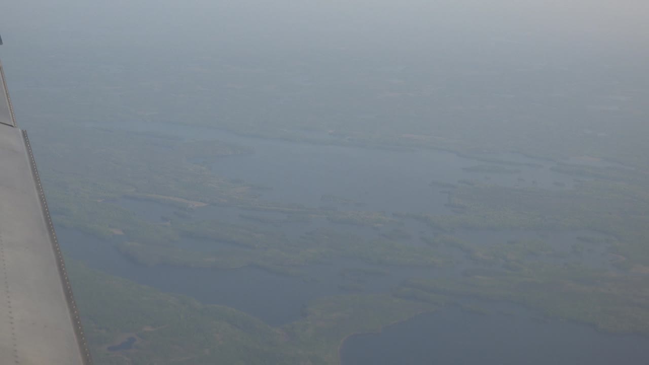 Wing edge and distant lakes seen through atmospheric haze.