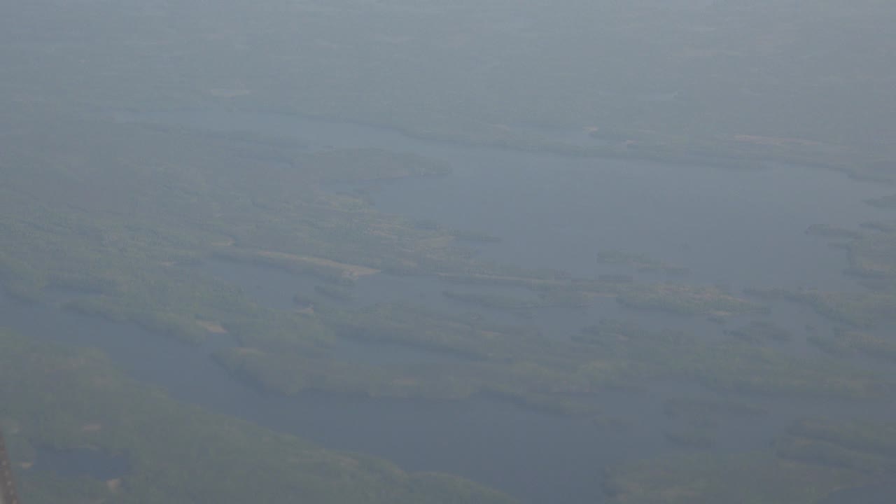 Hazy airplane-window view over Red Lake, Canada, showing blue-gray water, scattered forested landforms, and no visible people.