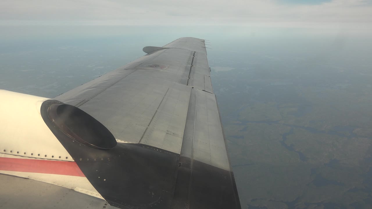 Plane wing and cloudy horizon over land.