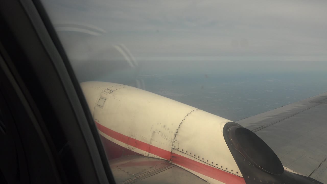 Airplane wing and engine viewed through window with water beyond.