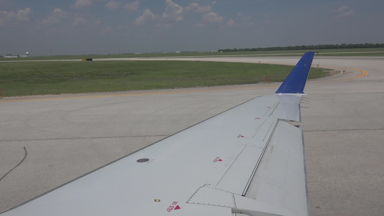 Blue-tipped airplane wing with broad runway pavement and grass.