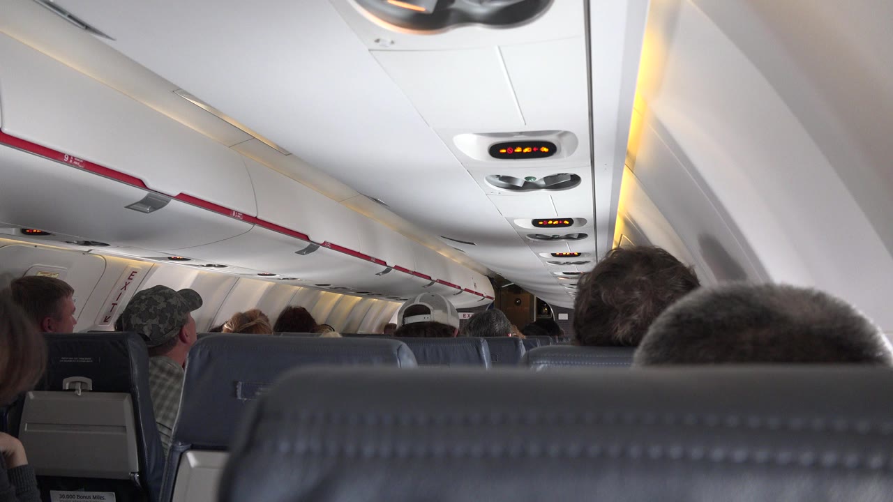 Passenger view down an airplane cabin with seats and overhead lights.