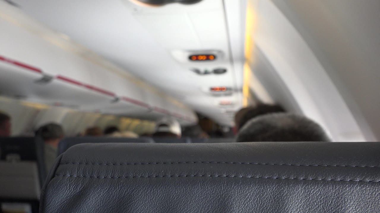 Winnipeg Canada 2015 cabin frame with a dark gray seatback across the lower edge, soft-focused passengers ahead, and warm indicator lights along the ceiling.