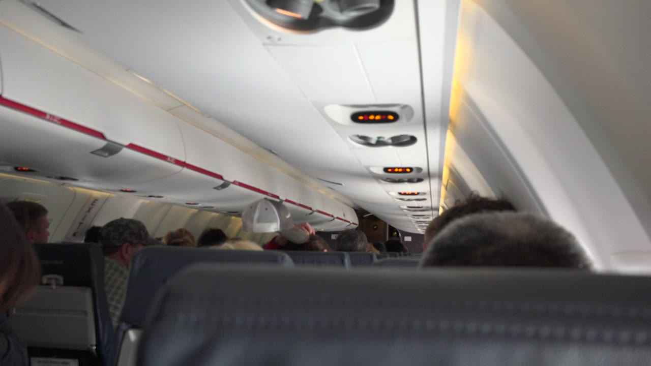Airplane cabin viewed over a seatback with passengers ahead.