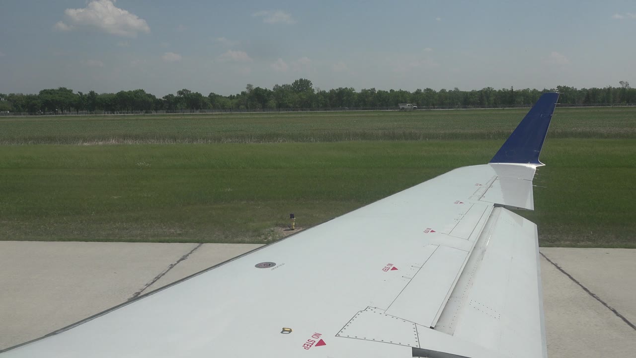 Blue-tipped airplane wing beside runway and open field