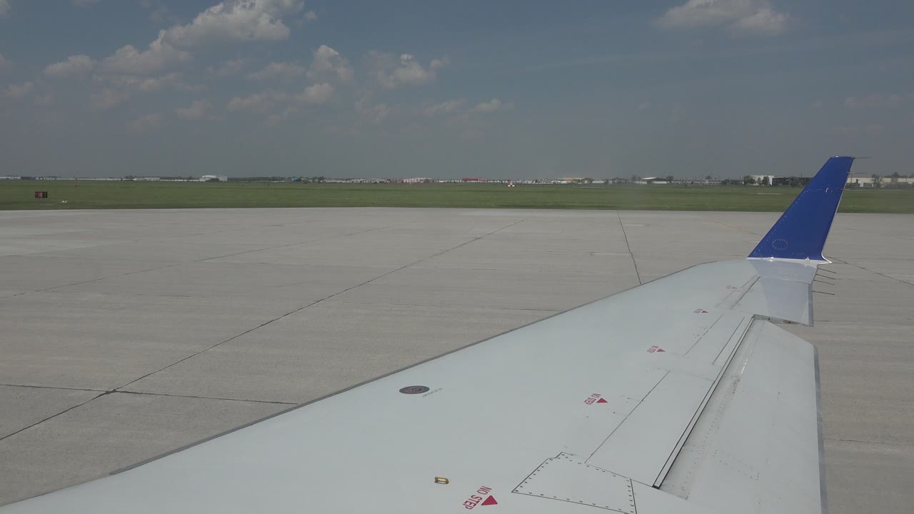 Airplane wing seen from a passenger window above gray tarmac.