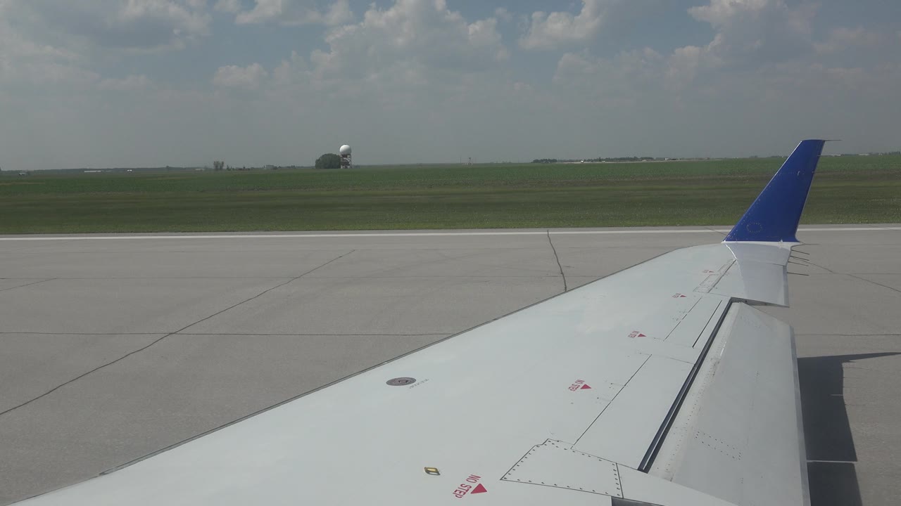Airplane wing seen from window with runway and distant field.