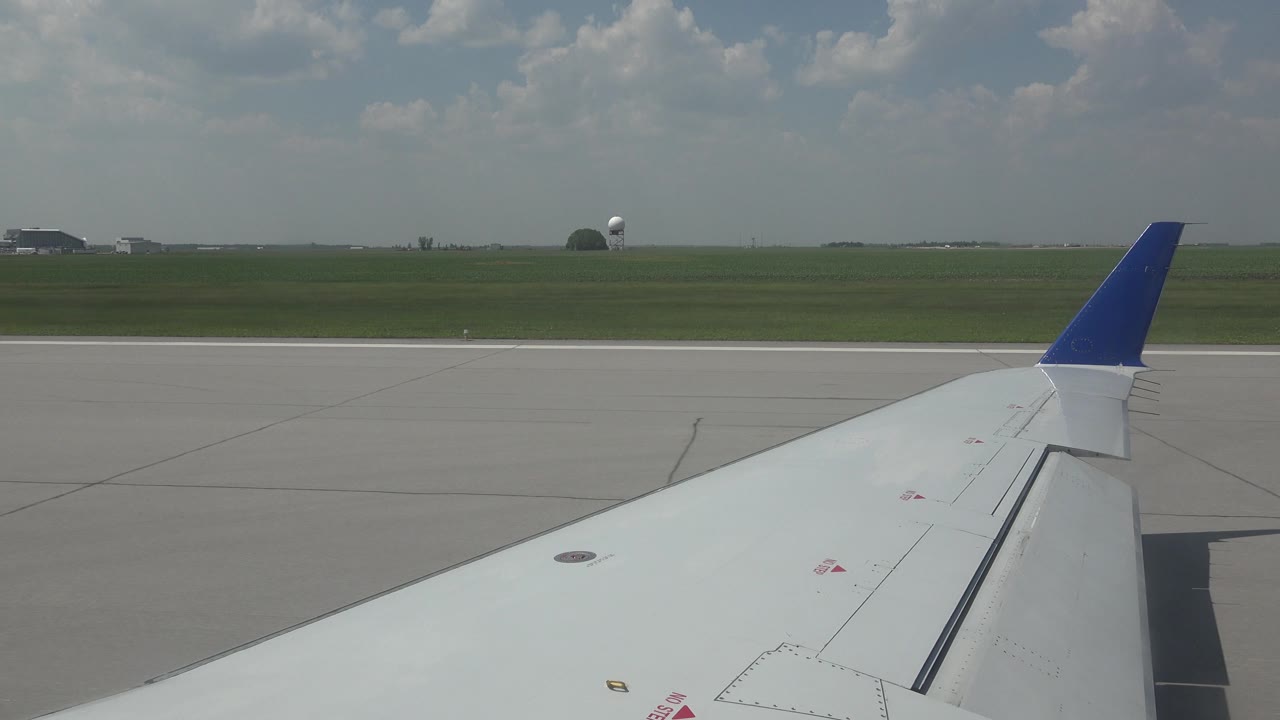 Airplane wingtip over runway with open grass beyond.