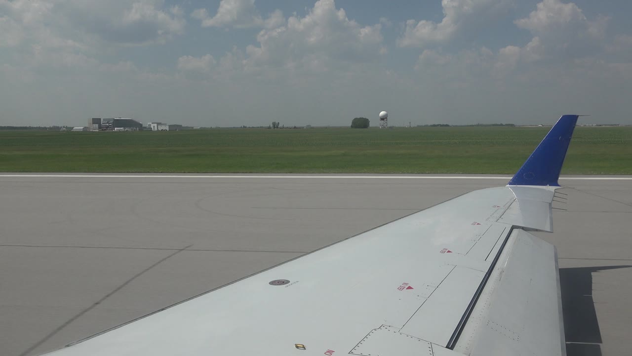 Aircraft wing over airport runway under scattered clouds.