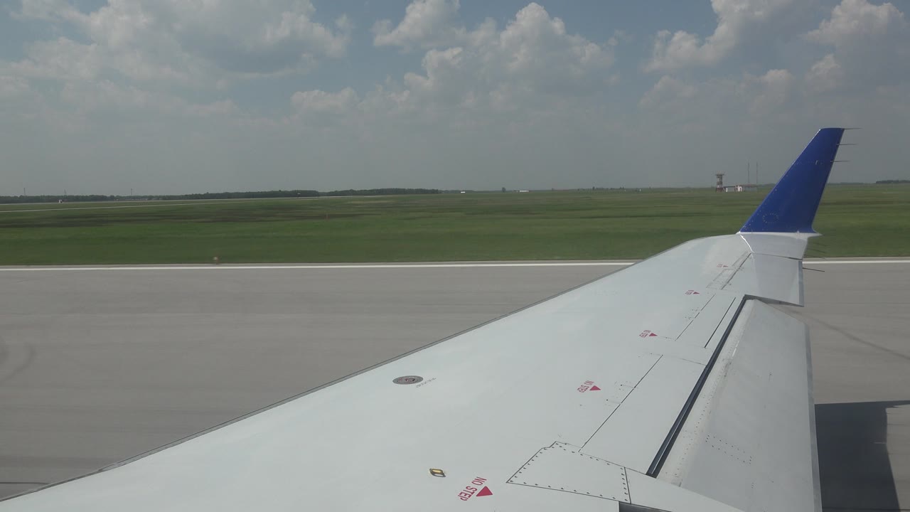 Airplane wingtip crossing runway and open grass field