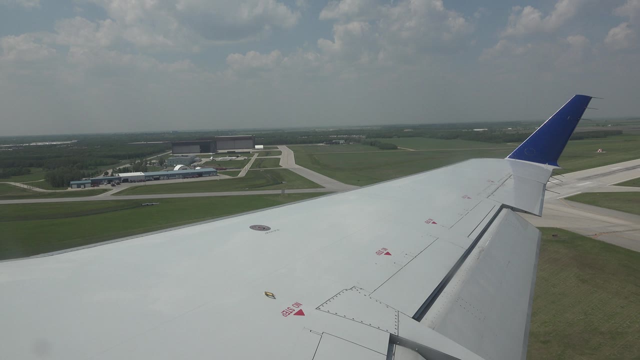 Plane wing over runway and open fields during takeoff.