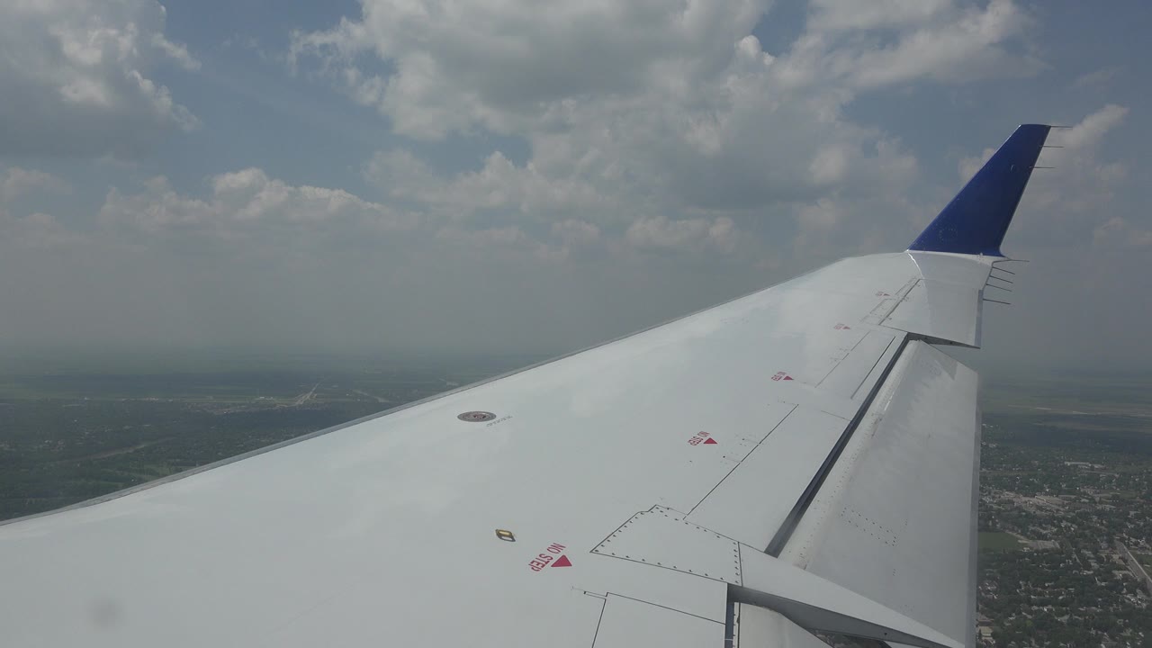 White airplane wing with blue wingtip above distant land and clouds