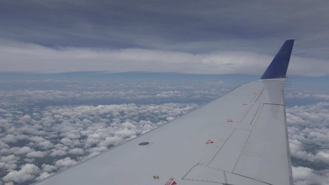 Opening frame of Winnipeg, Canada flight footage with a white airplane wing and blue wingtip over dense clouds under a darker cloud layer, no visible people.