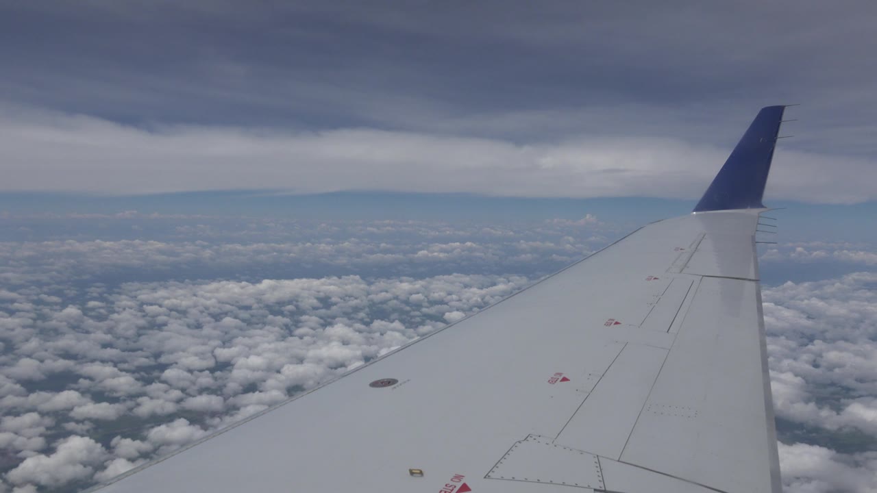 Winnipeg, Canada airplane-window view with the wing slightly farther across the frame, white clouds below, blue horizon beyond, and no visible people.