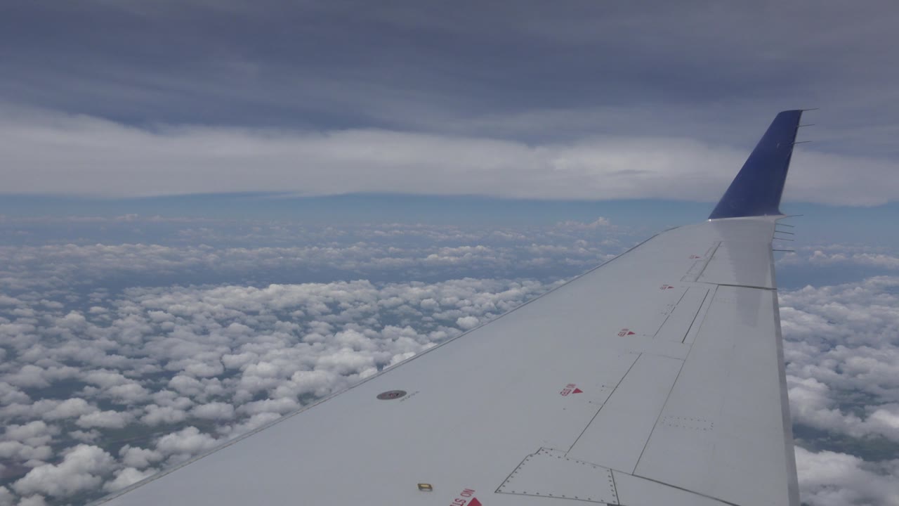 Plane wing crossing a cloudscape beneath darker sky