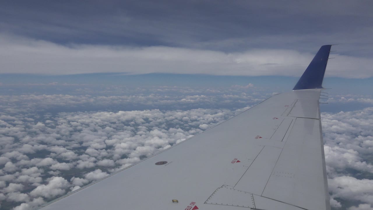Opening frame from Winnipeg, Canada footage showing a white airplane wing with a blue winglet over dense clouds, darker cloud cover overhead, and no visible people.