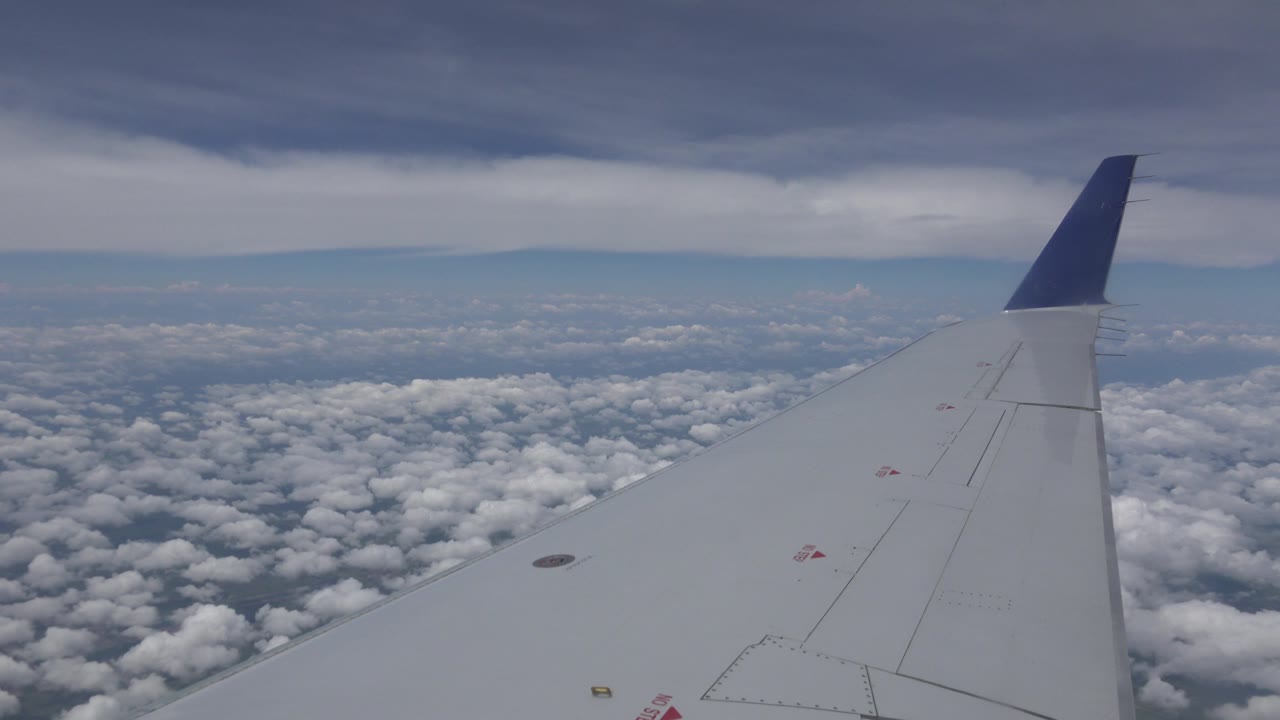 Airplane wing and blue winglet over cloud tops.