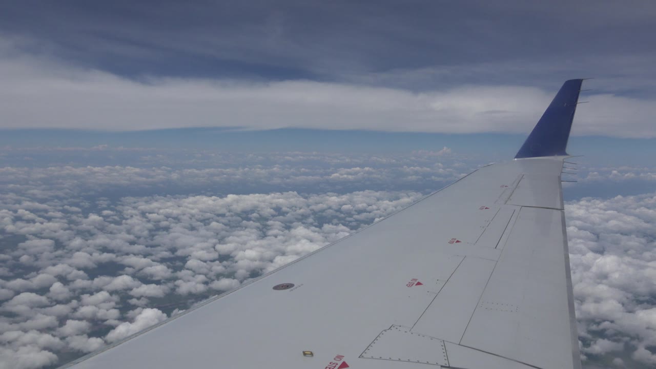 Start of the Winnipeg, Canada flight view, with a gray airplane wing and dark blue winglet over white clouds, a pale horizon, and no visible people.