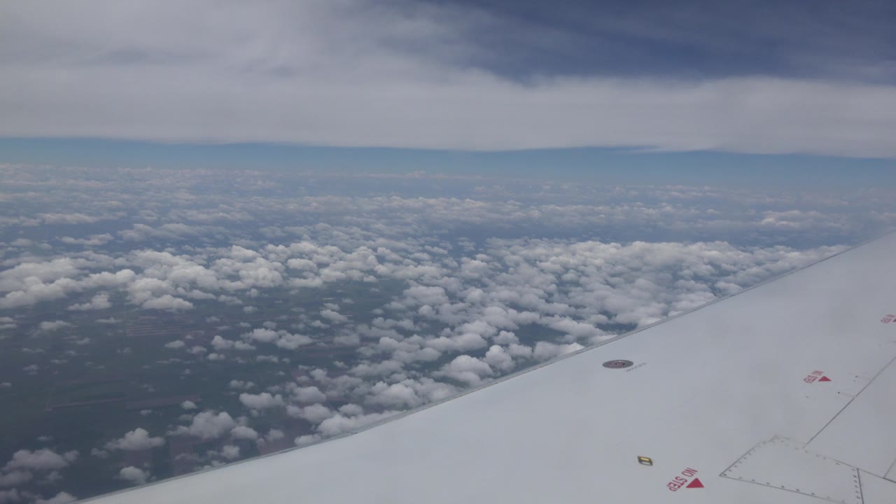 A white airplane wing angles across the lower right as broken clouds spread over the landscape near Winnipeg, Canada, with no visible people.