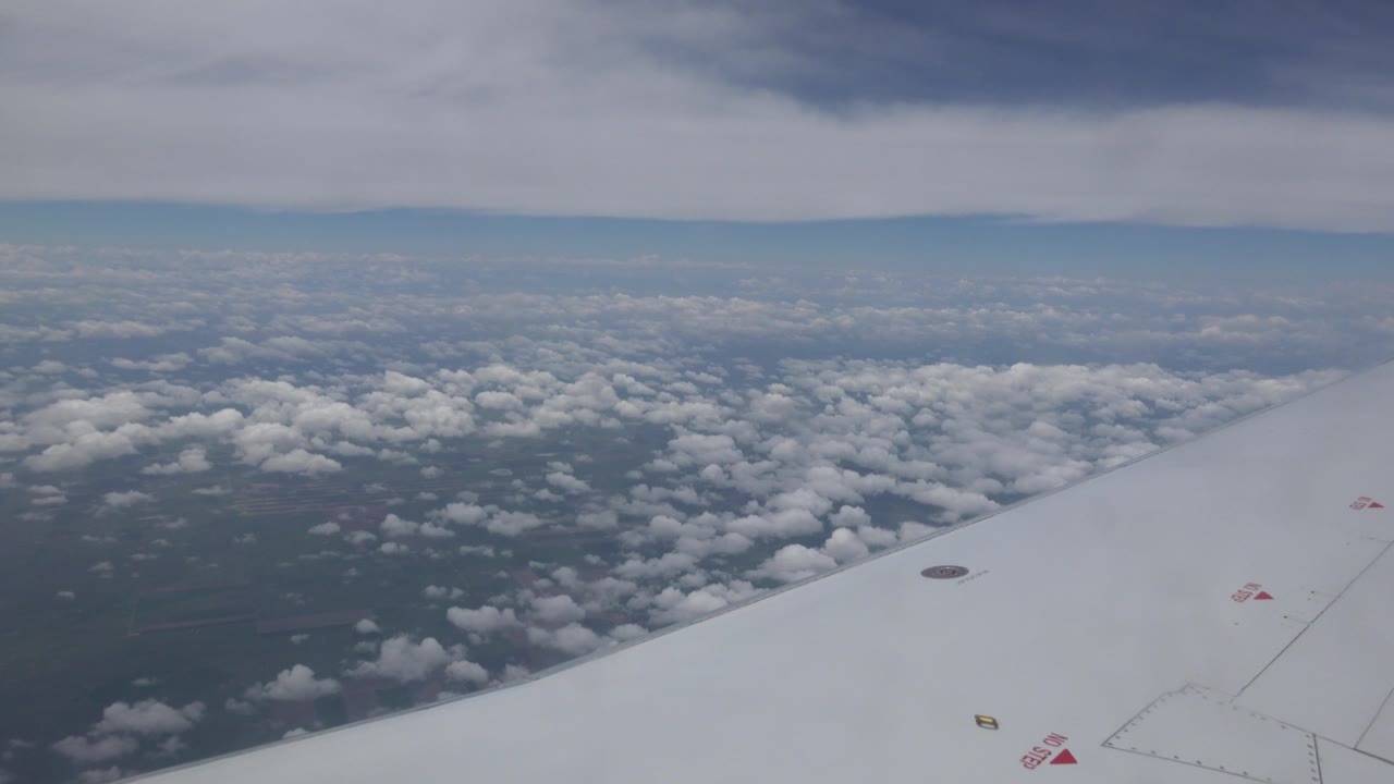 White airplane wing seen from a passenger-window angle above Winnipeg, Canada, with scattered clouds below, a pale horizon, and no visible people.