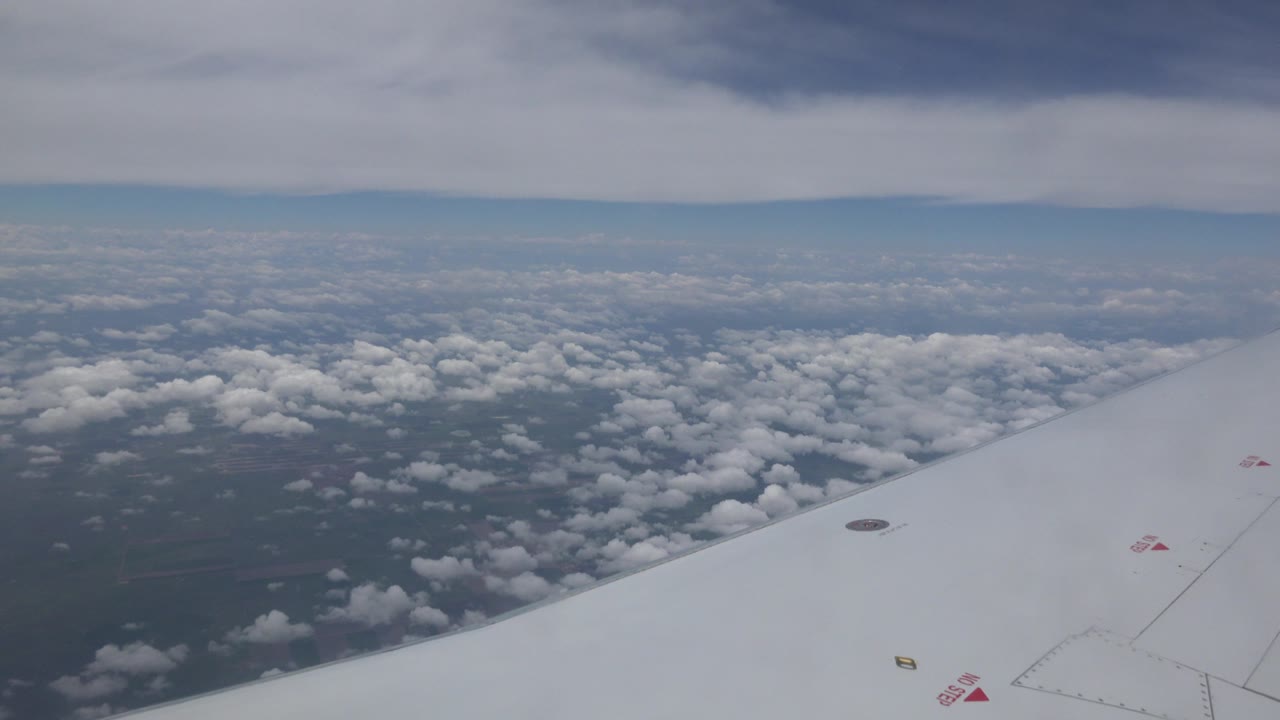 Passenger-window view over Winnipeg, Canada, with the white wing extending into the frame, broken clouds over dark ground, and no visible people.