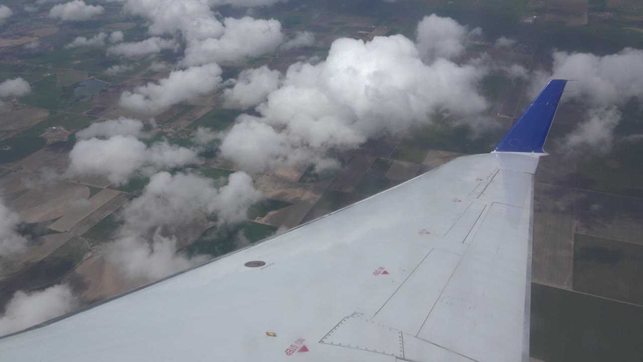 Airplane wingtip above cloudy farmland.