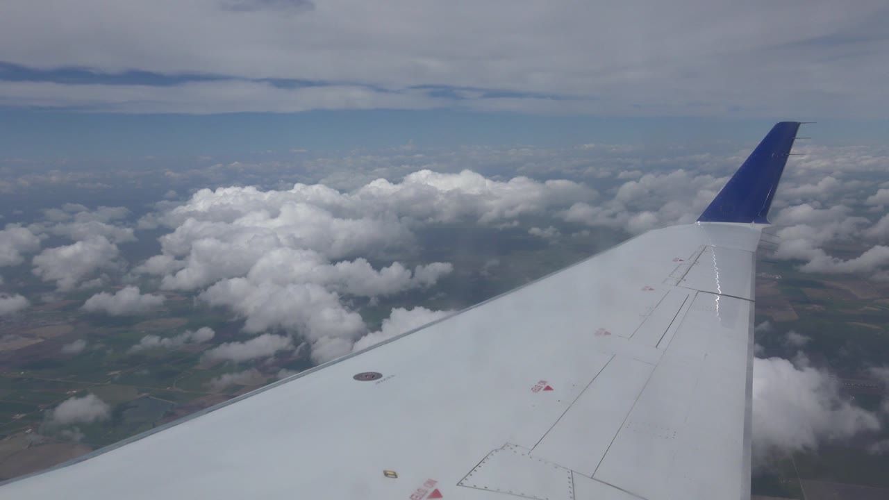 Airplane wing above clouds and distant ground