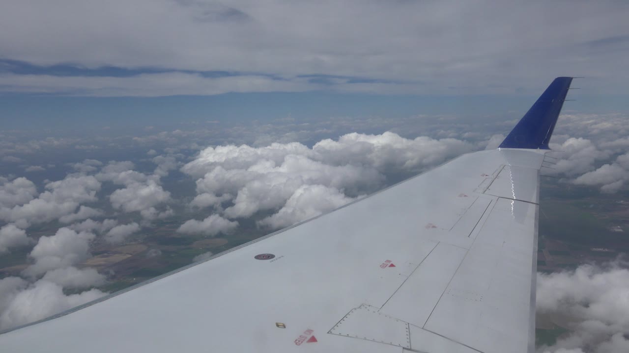 The airplane wing remains diagonal in frame as bright cloud banks sit beyond it over the Winnipeg, Canada flight path, with no visible people.