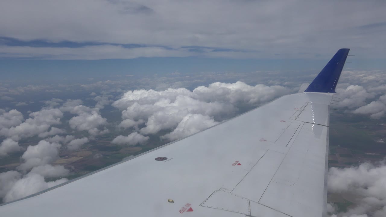 Blue-tipped aircraft wing over white clouds