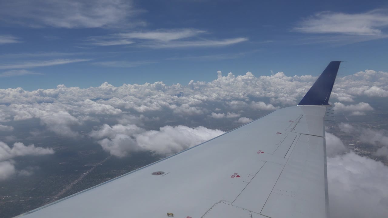 In-flight view near Winnipeg, Canada with the airplane wing centered below a broad cloud bank, patches of land visible through haze, and no visible people.
