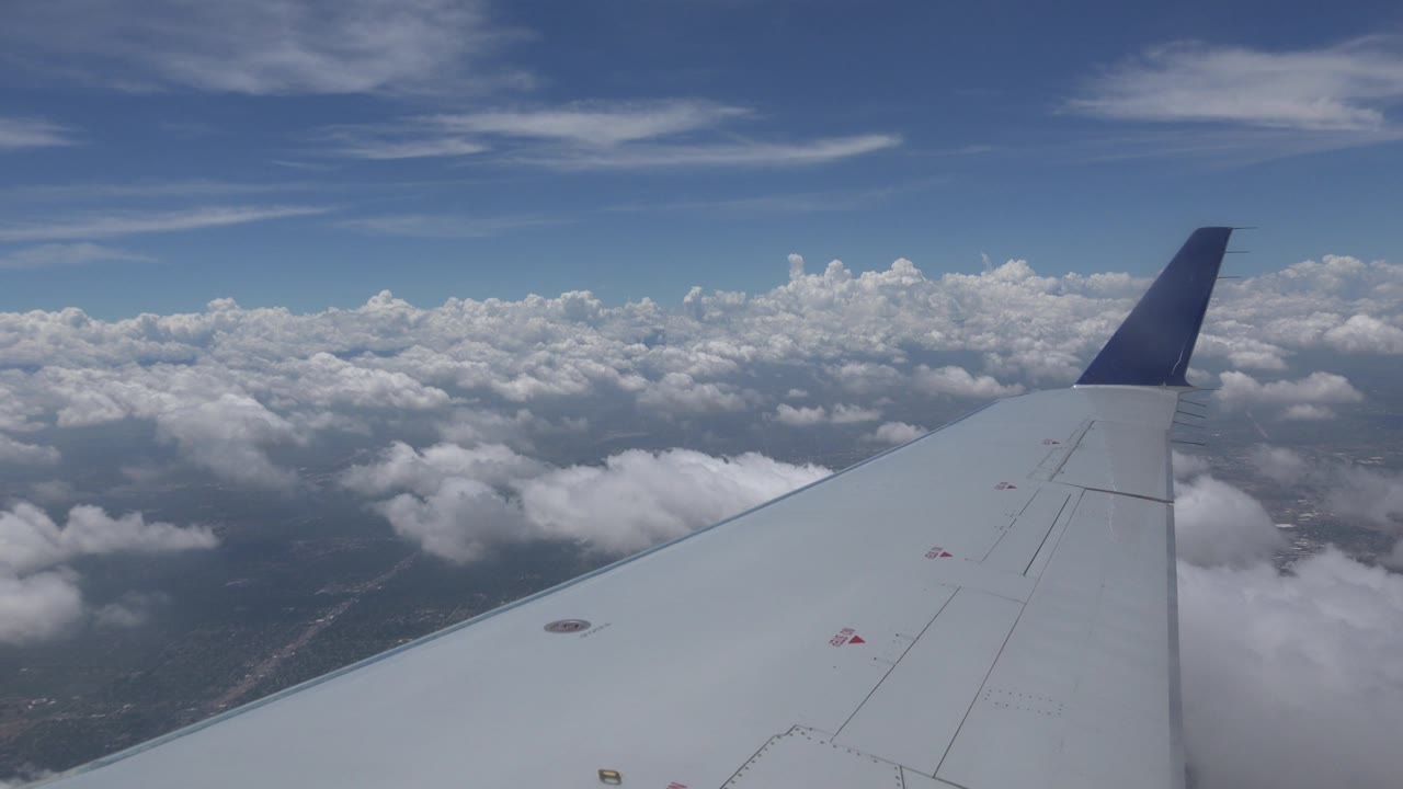 Airplane wing over broken clouds and ground