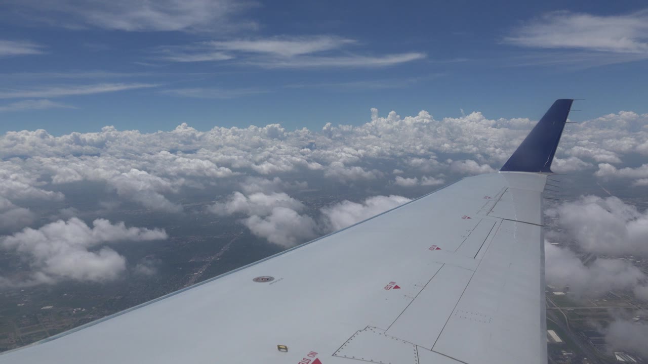 White airplane wing and dark blue winglet over scattered clouds and distant ground near Winnipeg, Canada, with no visible people.