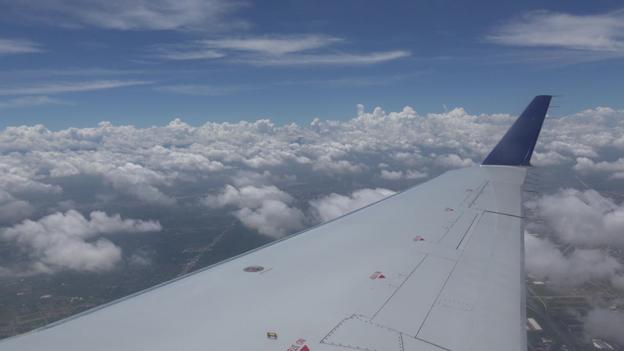Airplane wing remains centered over layered white clouds, with patches of ground visible below in the Winnipeg, Canada flight view and no visible people.
