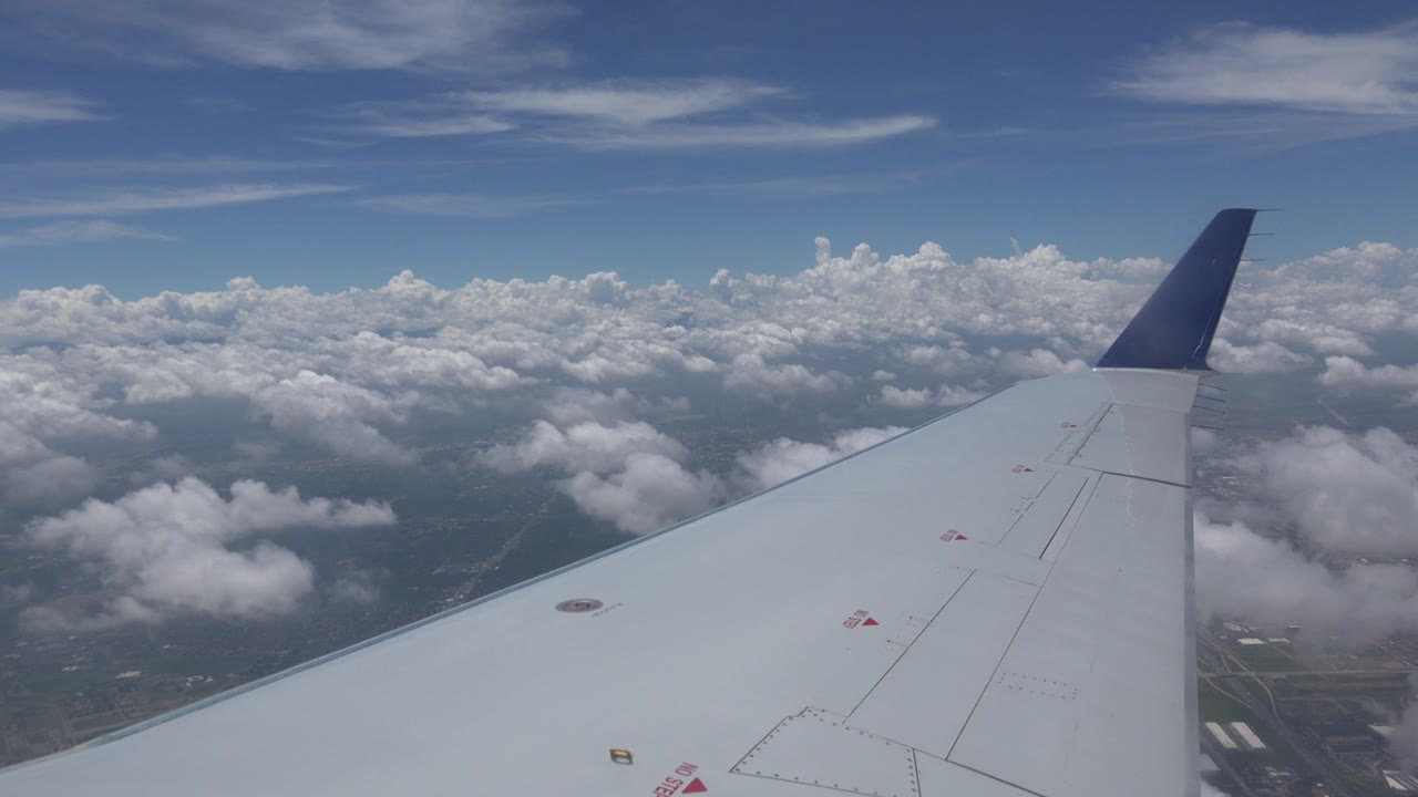 Airplane wingtip against blue sky and white cloud tops.