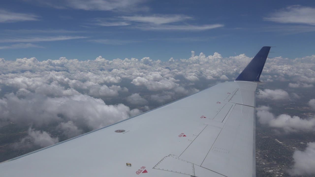 Airplane wing above cloud cover and blue sky.