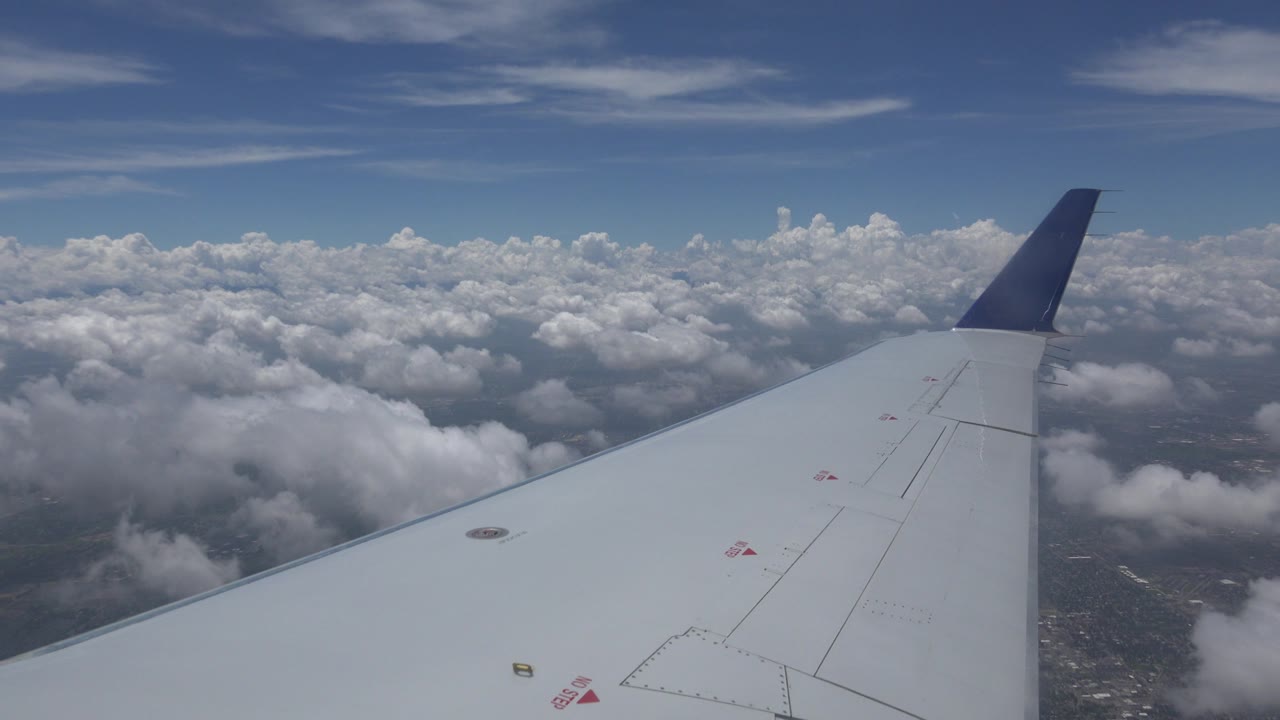 The airplane wing stretches diagonally across the frame above broken clouds and faint land below near Winnipeg, Canada, with no visible people.