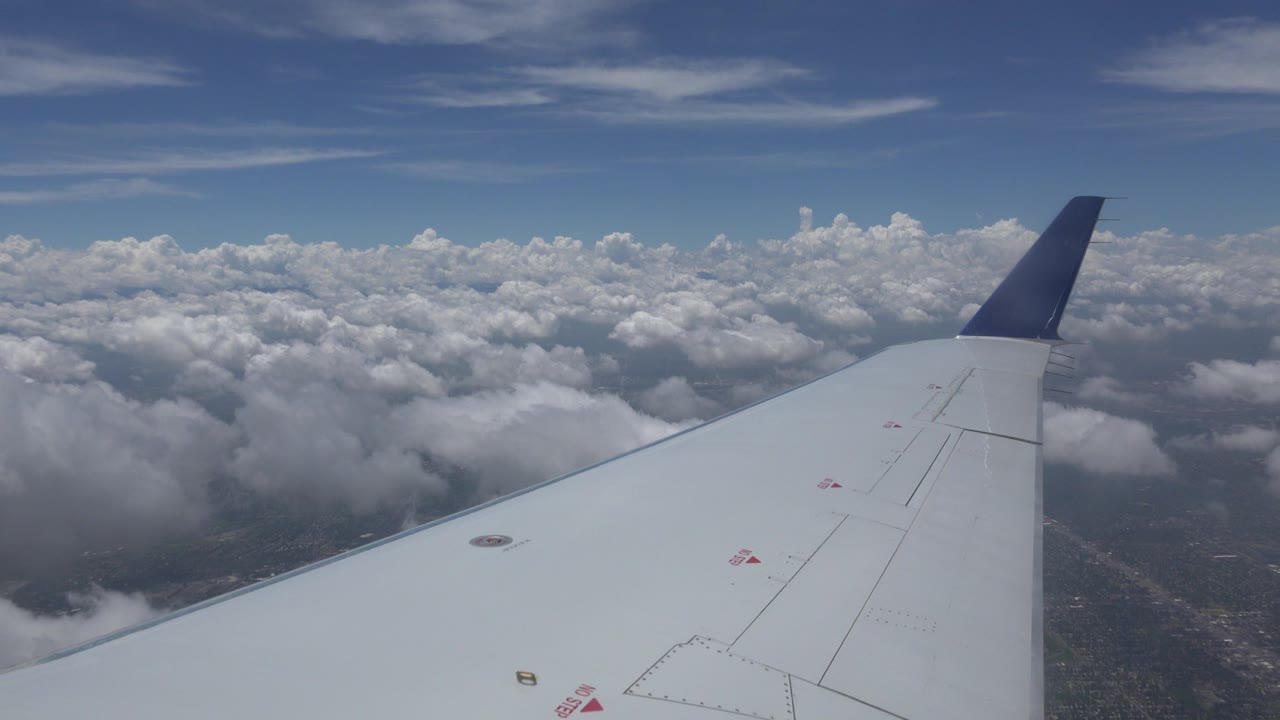 At 0:00, a white airplane wing with a dark blue tip extends over layered clouds near Winnipeg, Canada, with no visible people.