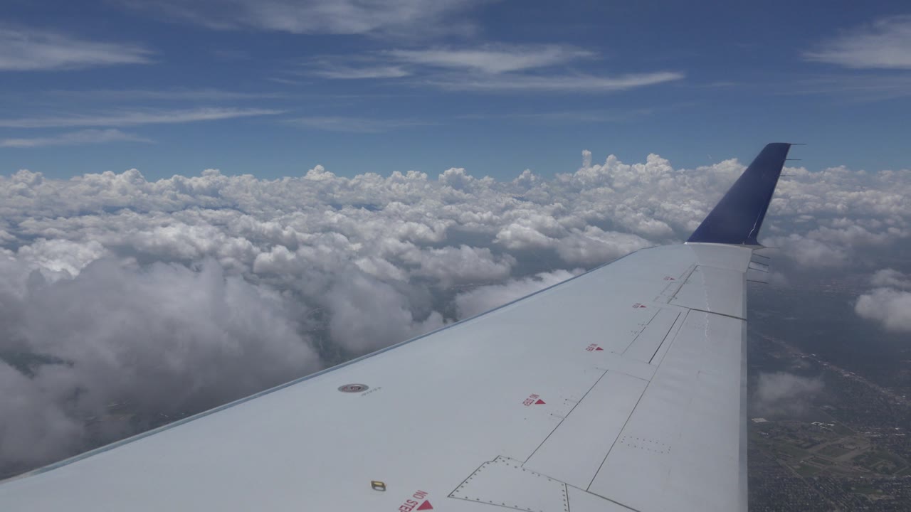 Aircraft wing with clouds and distant ground below.