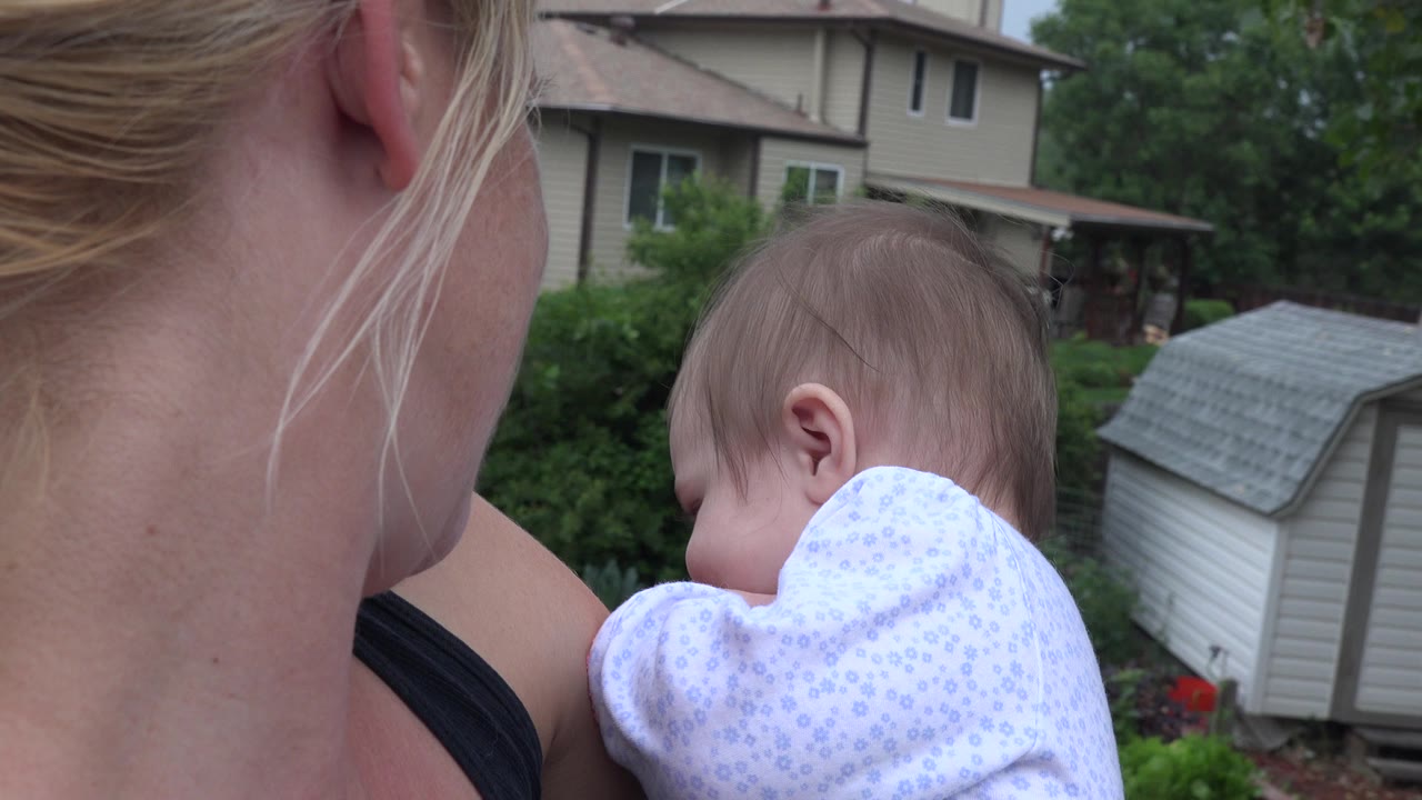 Woman holding a baby while looking across a backyard.