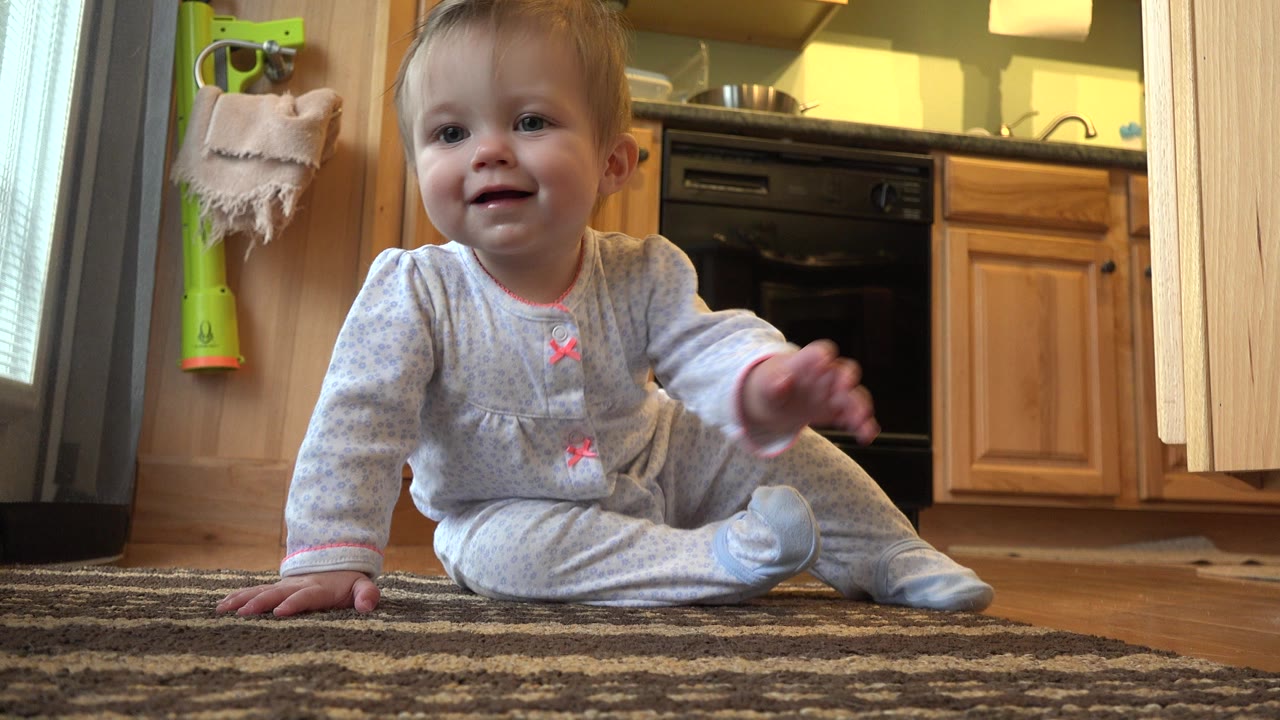 Toddler sitting on a rug in a kitchen.