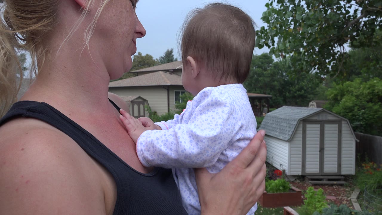 Woman holding a baby in a backyard near a shed