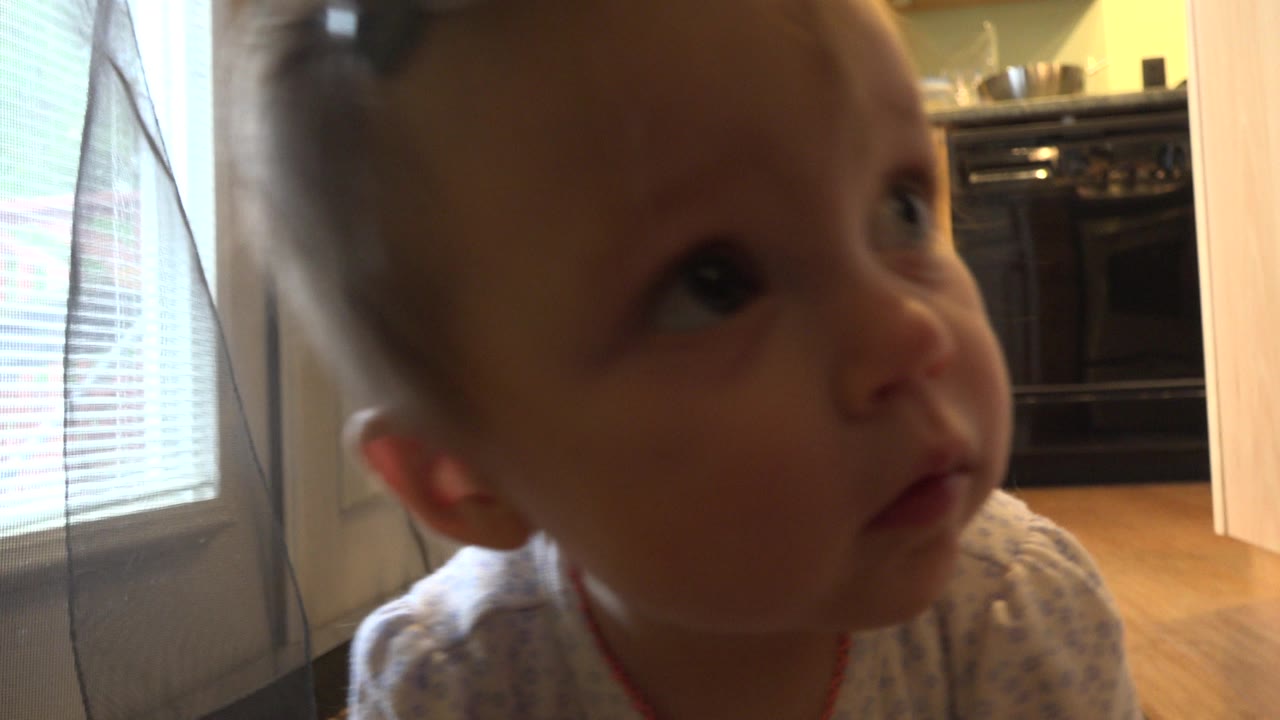 At 0:01, the baby remains close to the lens in the Westminster, Colorado home interior, looking upward with the glass door and kitchen still behind.