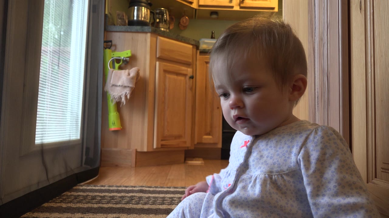 Blonde baby sitting on a rug near a kitchen doorway.