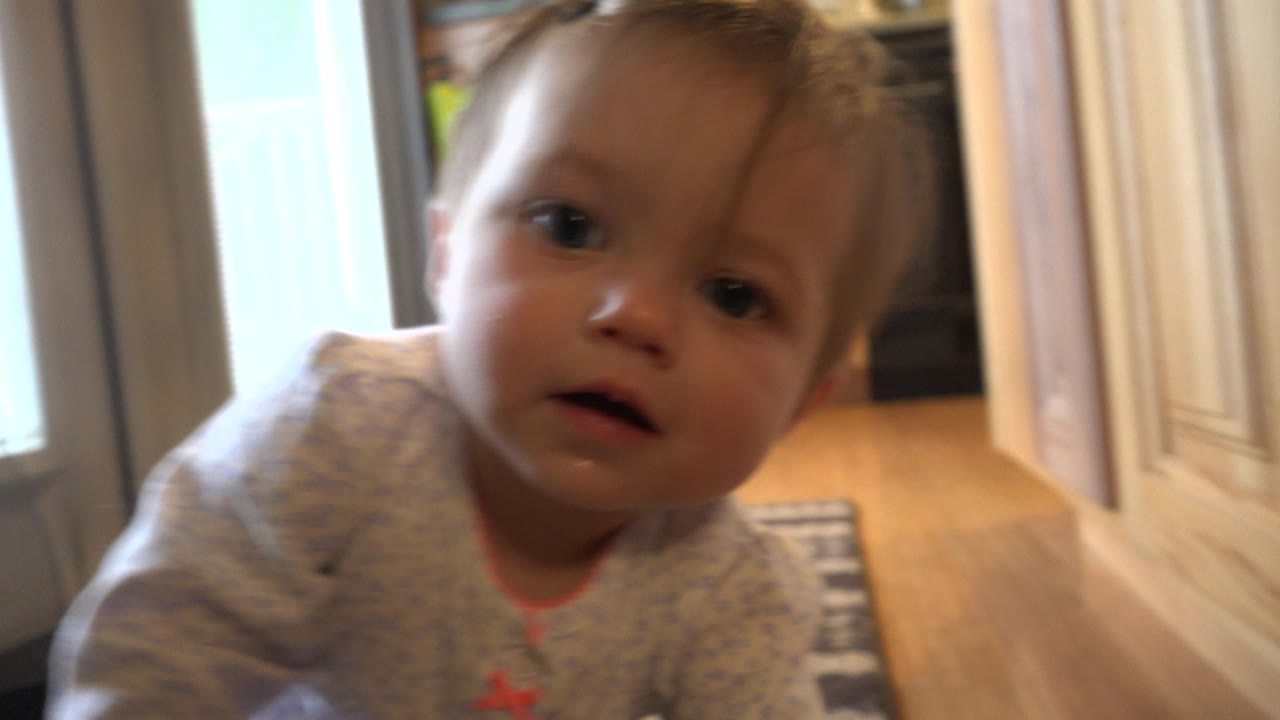 The toddler faces the lens more squarely in the Westminster, Colorado interior, with daylight from the glass door and kitchen cabinets in the background.